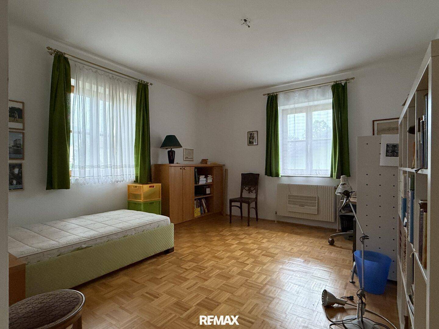 Schlafzimmer mit Parkettboden, zwei Fenstern und einem Einzelbett.