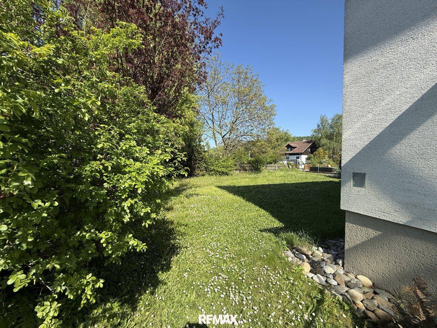 Großer Gartenbereich mit Rasen, Sträuchern und einem kleinen Steinbeet.