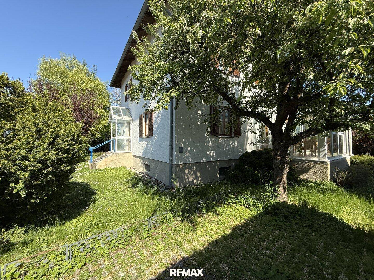 Seitenansicht des Hauses mit Wintergarten, umgeben von Bäumen und Grünflächen.