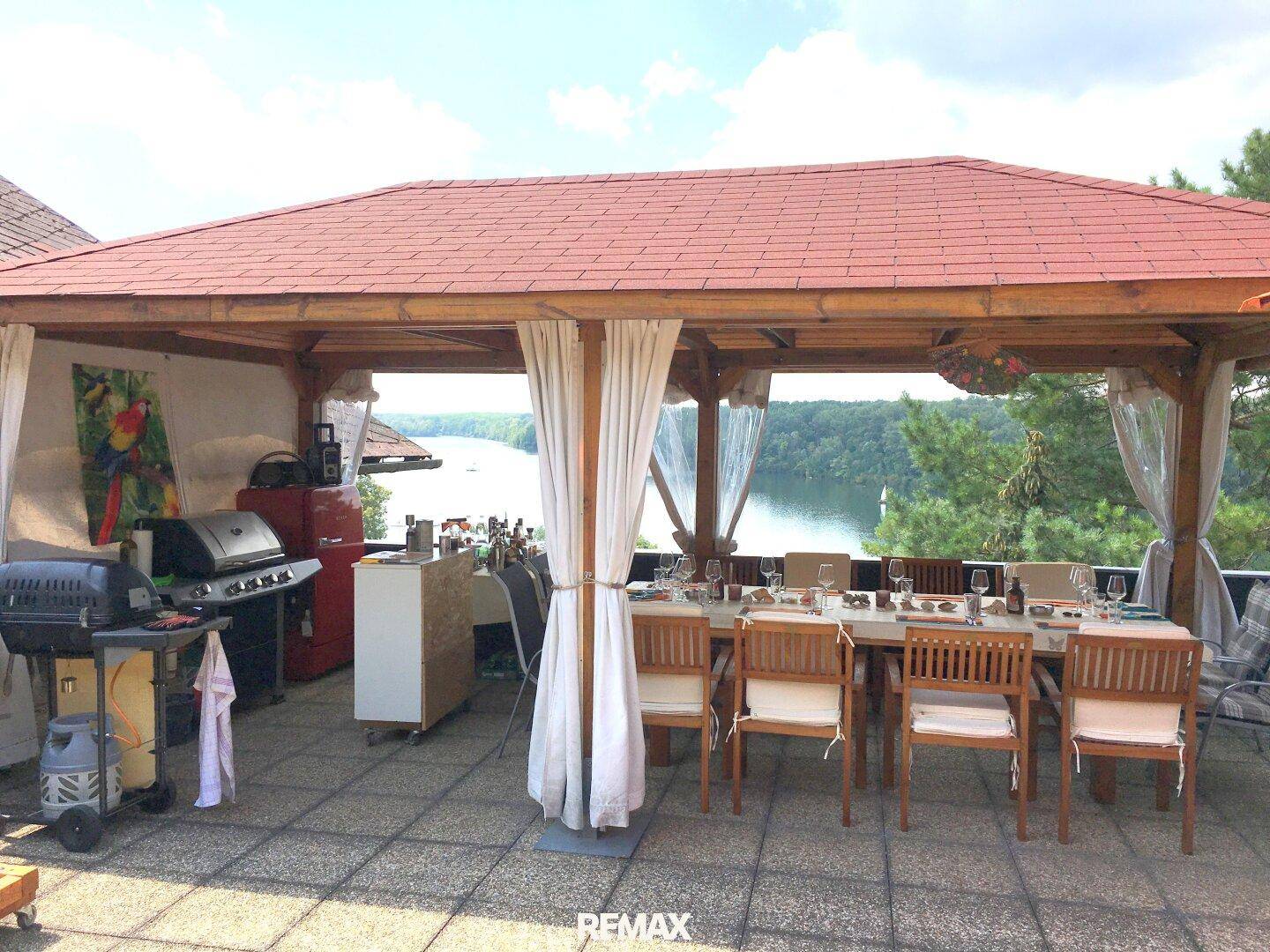 Große überdachte Terrasse mit Esstisch und Grillbereich, ideal für Mahlzeiten im Freien mit Seeblick.