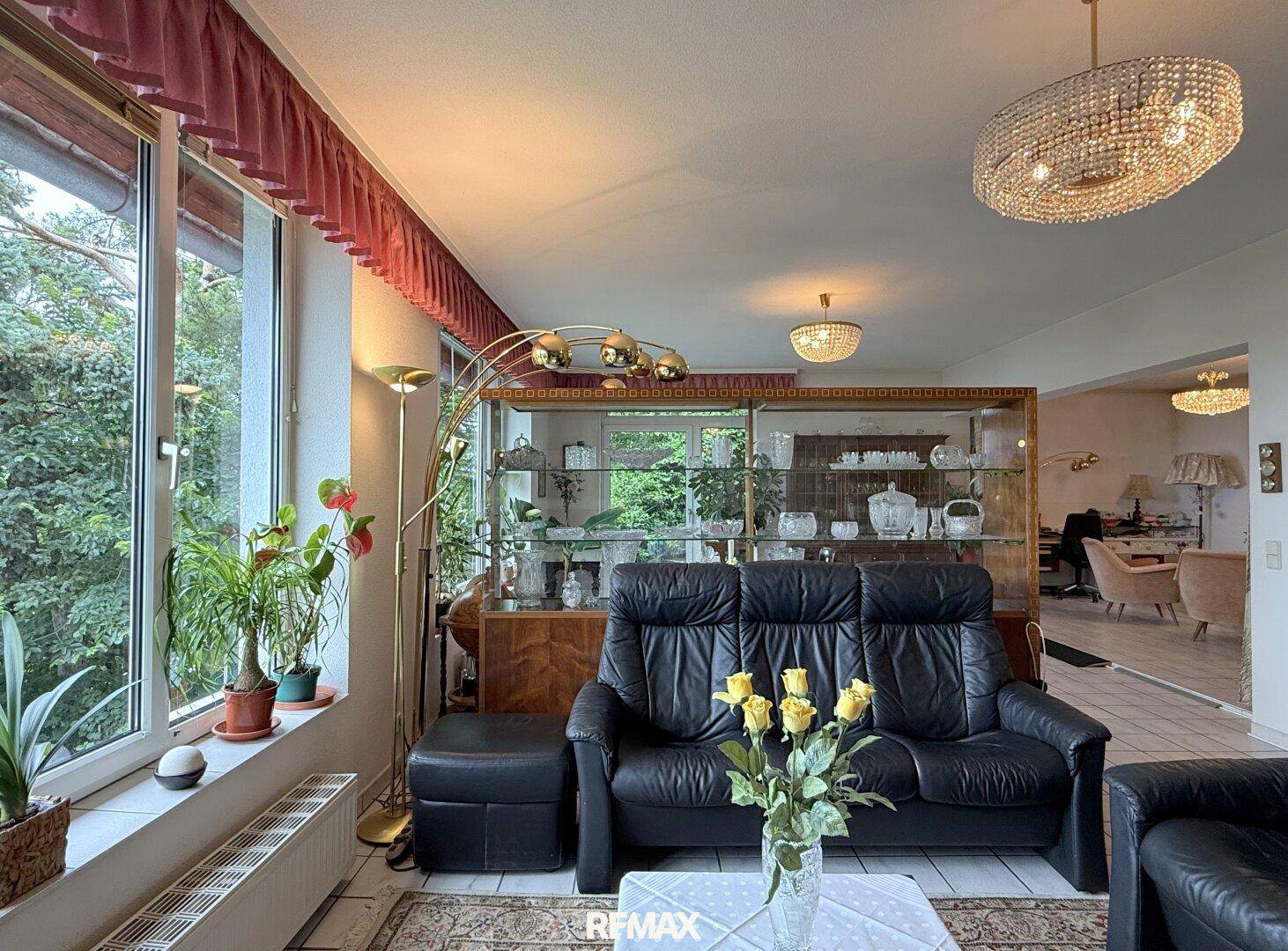 Gemütliches Wohnzimmer mit Ledersofa, Pflanzen und großen Fenstern mit Blick ins Grüne.