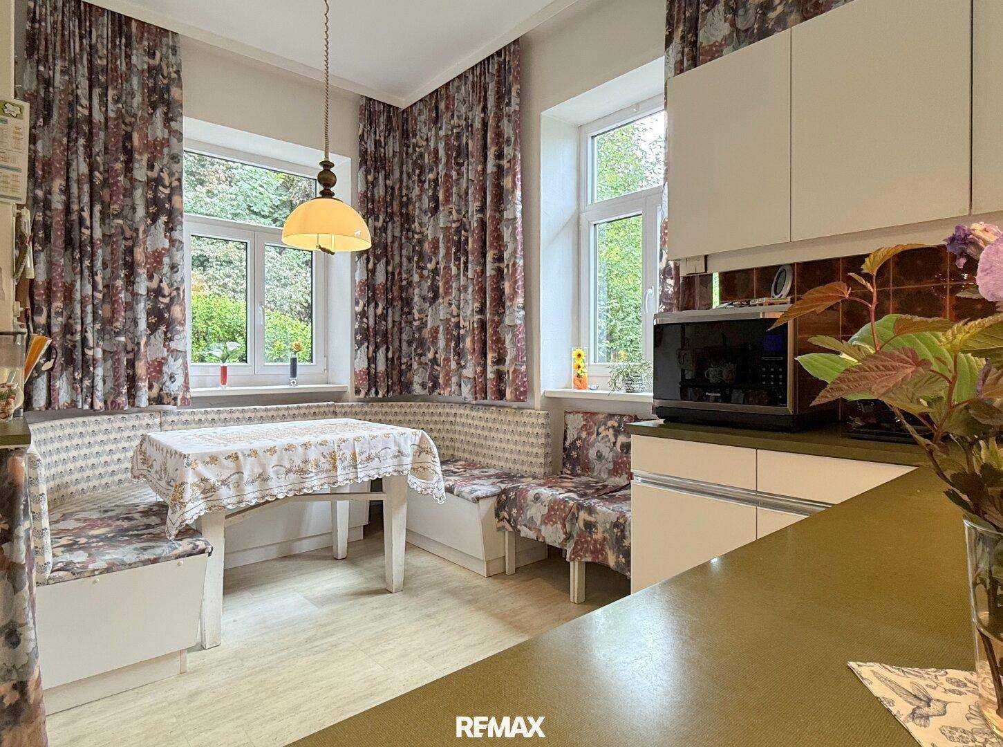 Gemütliche Küche mit Essecke, weißen Schränken und floralen Vorhängen.