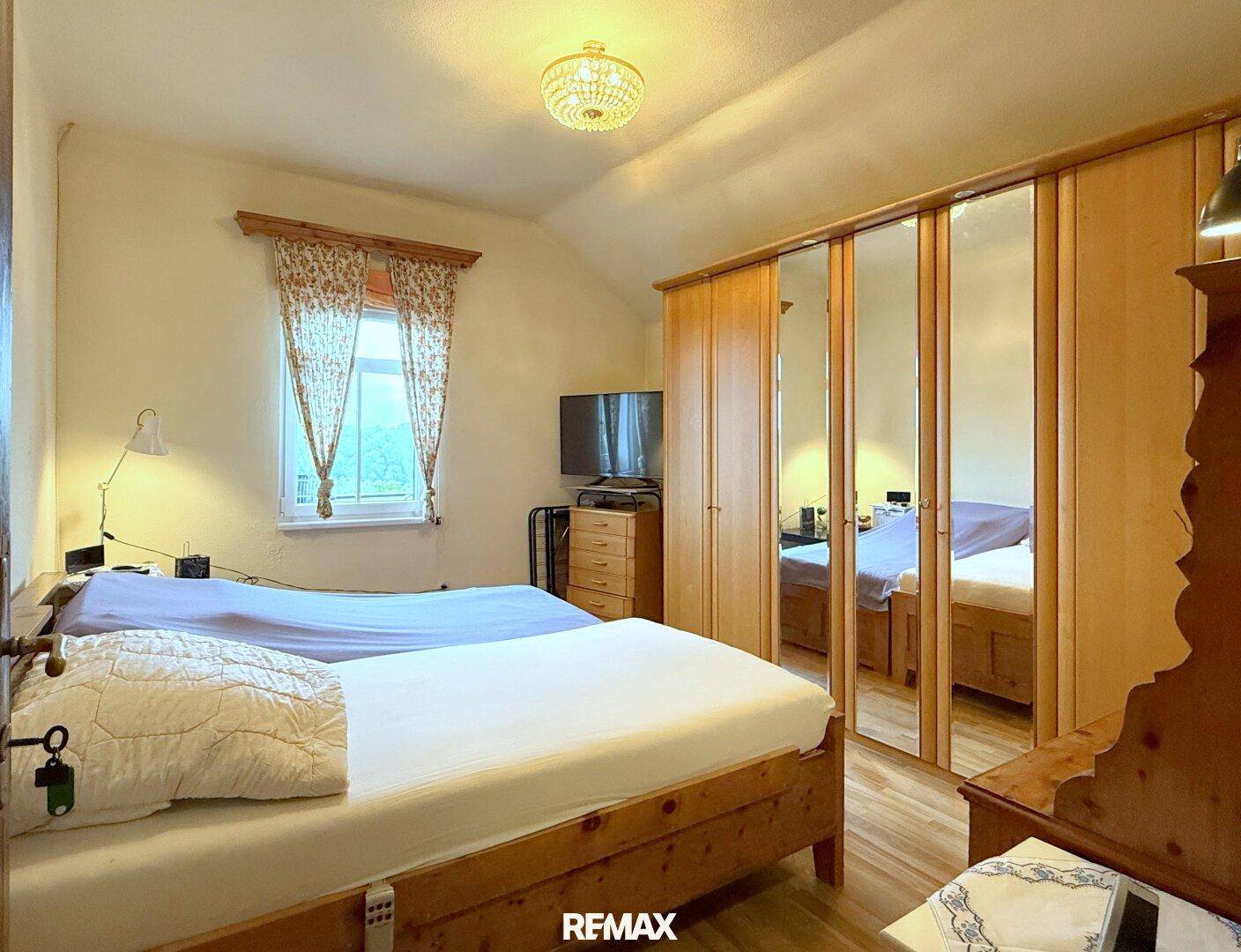 Schlafzimmer mit zwei Einzelbetten, Spiegelschrank und Fenster mit Blick ins Grüne.