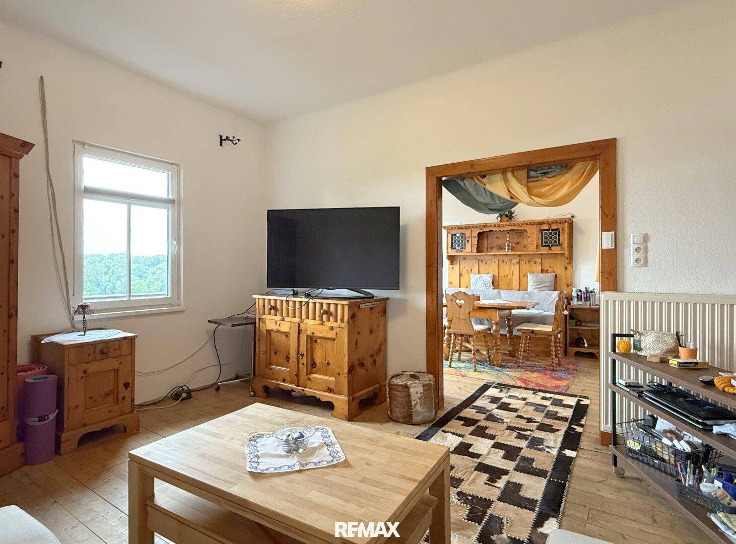 Wohnzimmer mit Holzboden, Fernseher und offenem Durchgang zum Essbereich.