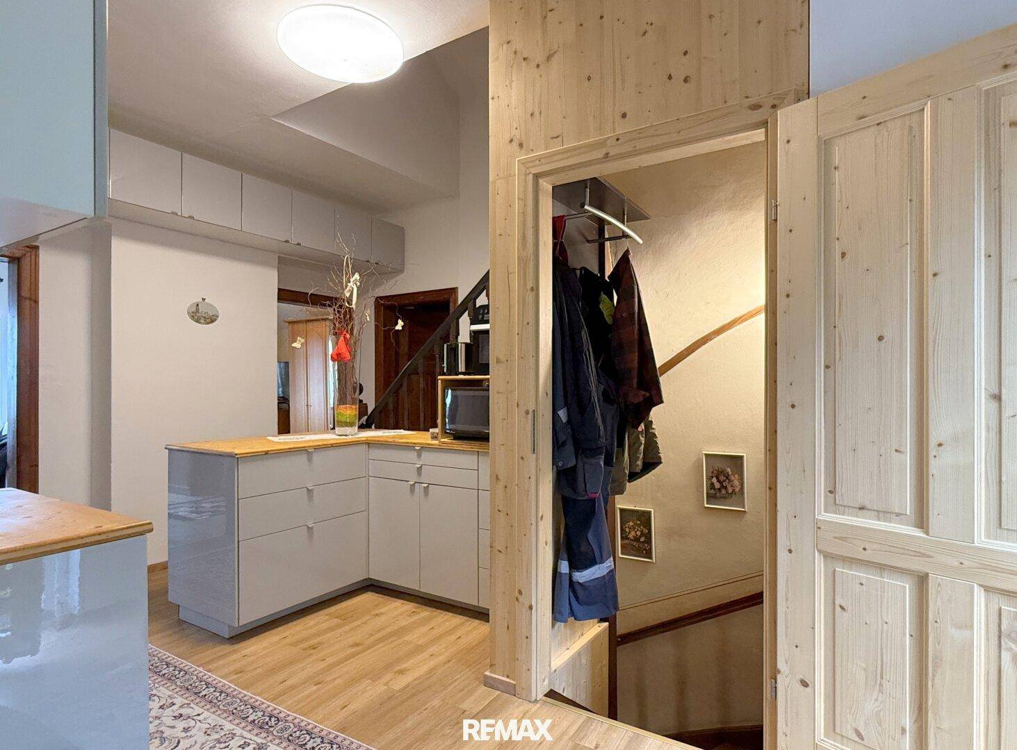 Eingangsbereich mit Garderobe, Holzvertäfelung und integrierter Küchenzeile unter der Treppe.