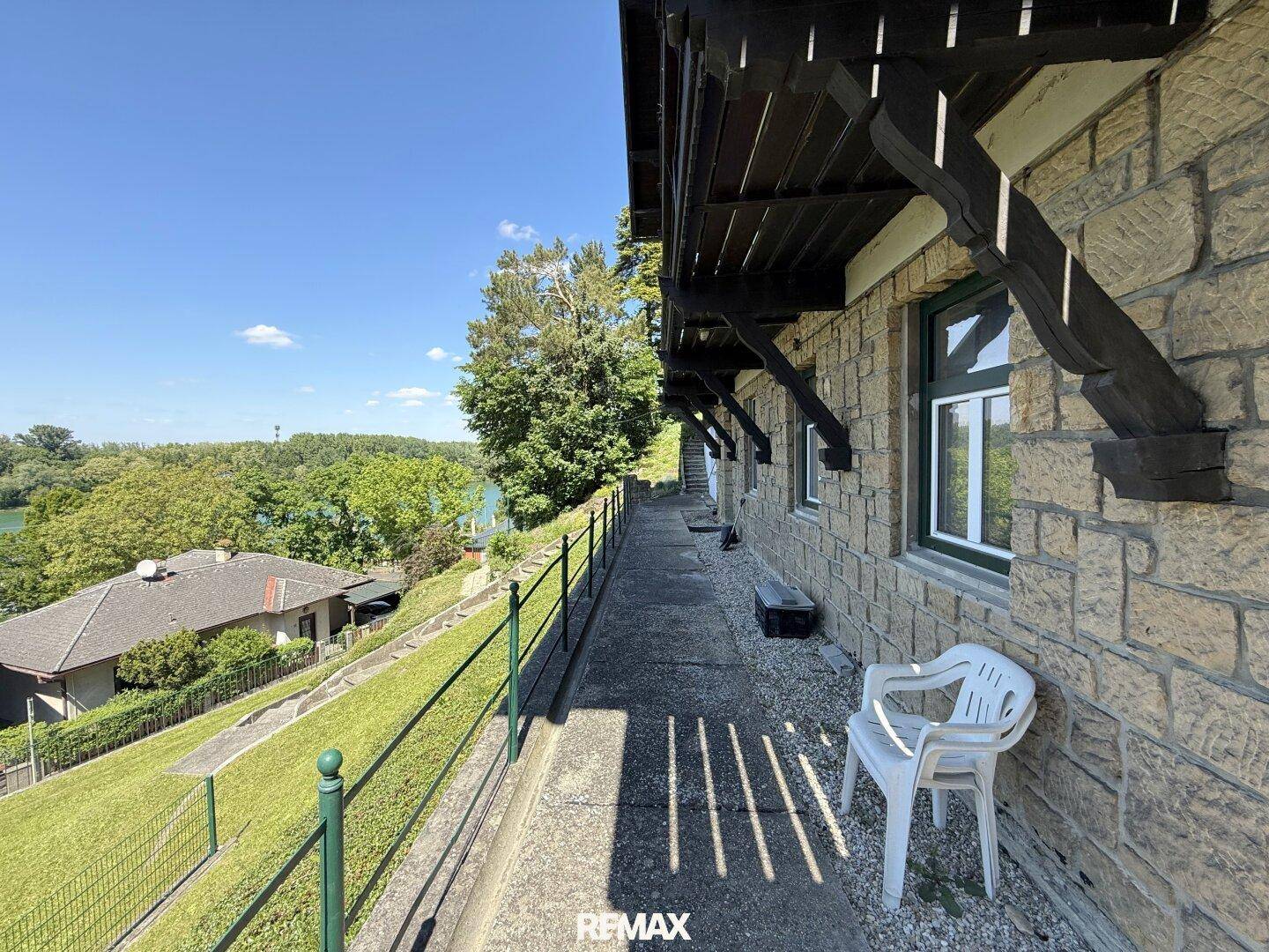 Langer Weg entlang des Hauses mit Steinmauer und weitem Seeblick.