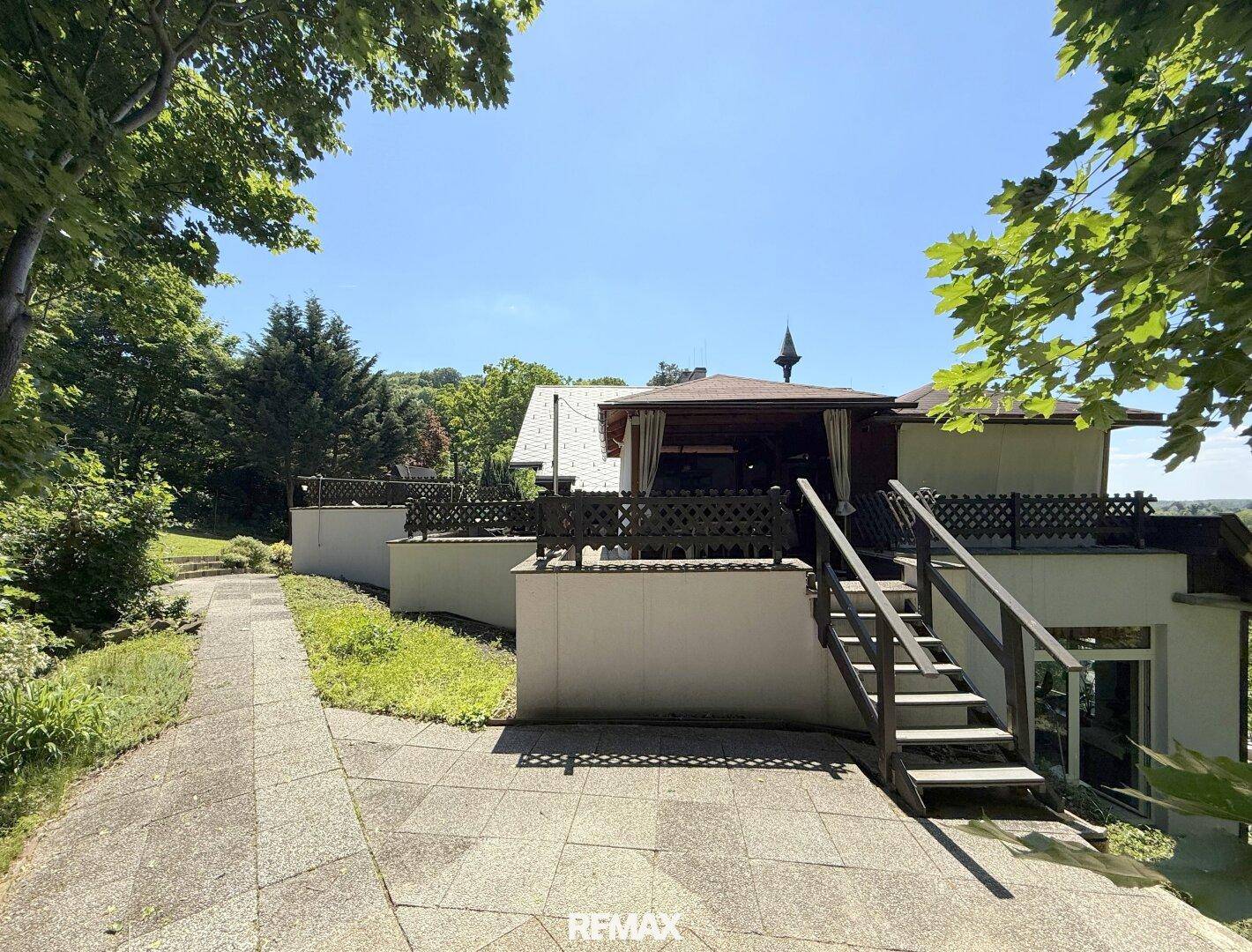Großer gepflasterter Außenbereich mit Treppe zu einer überdachten Terrasse.
