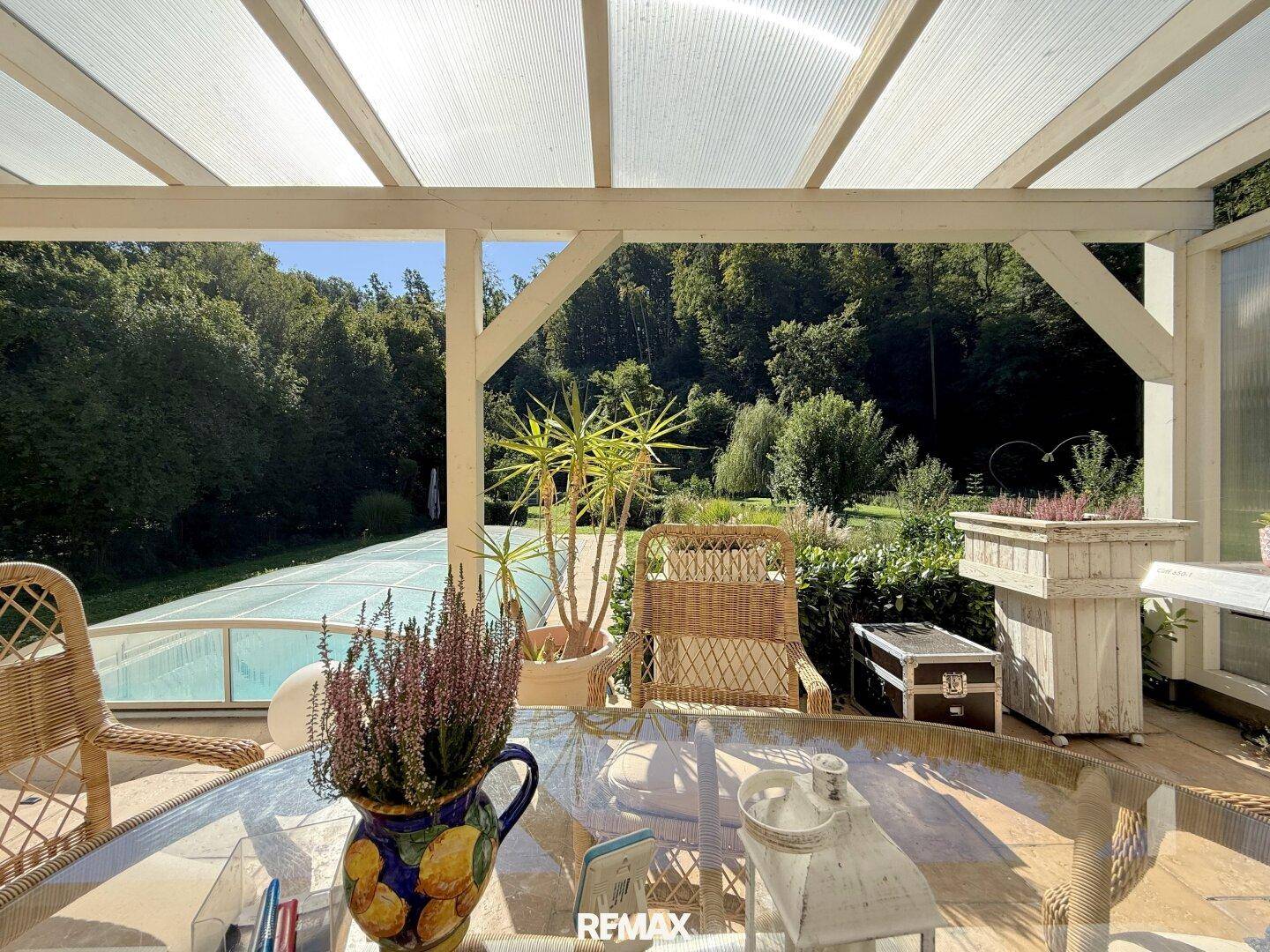 Überdachte Terrasse mit Gartenmöbeln und Blick auf den Pool und die grüne Umgebung.
