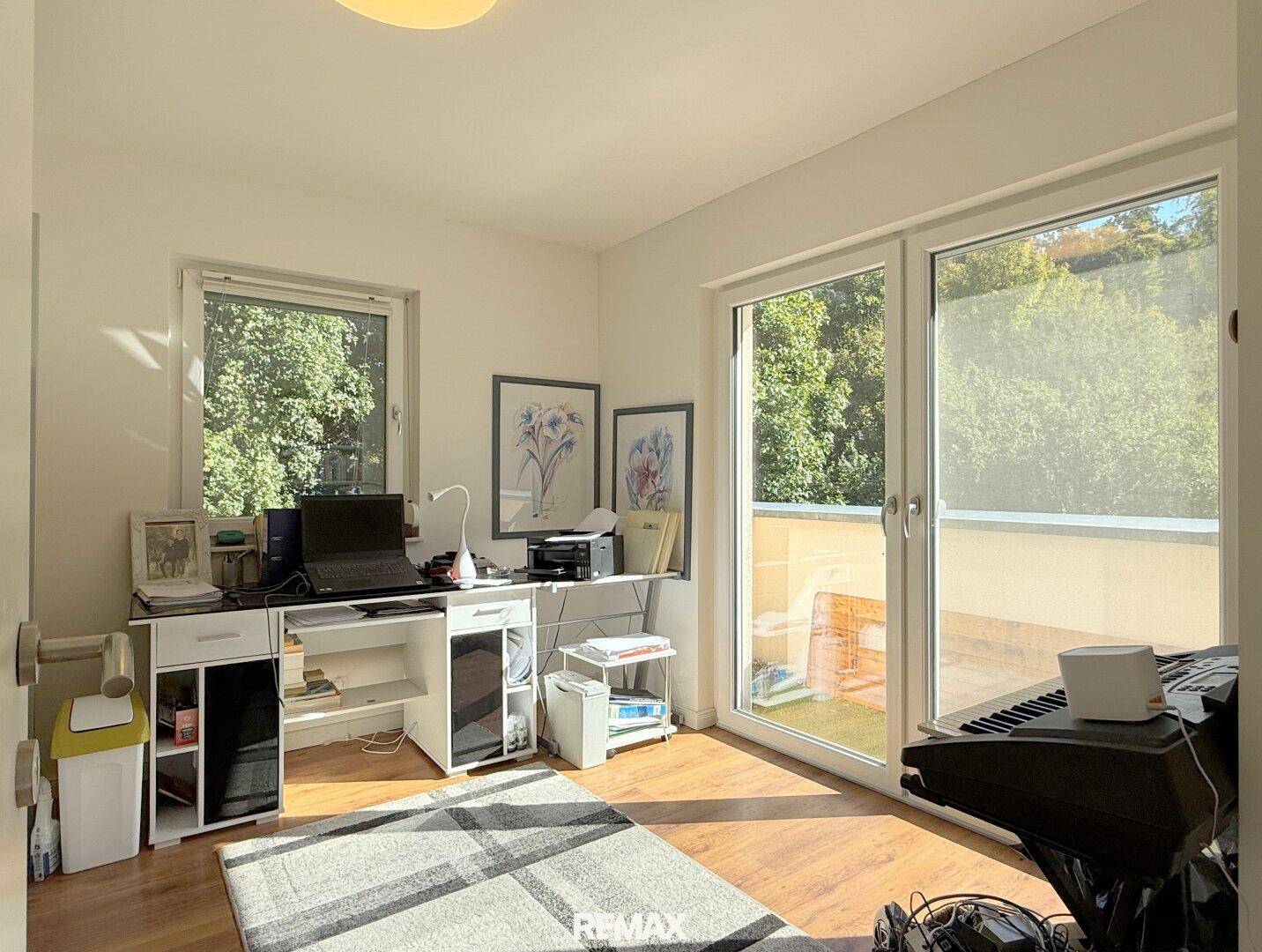Helles Arbeitszimmer mit Schreibtisch, Holzboden und Zugang zum Balkon.