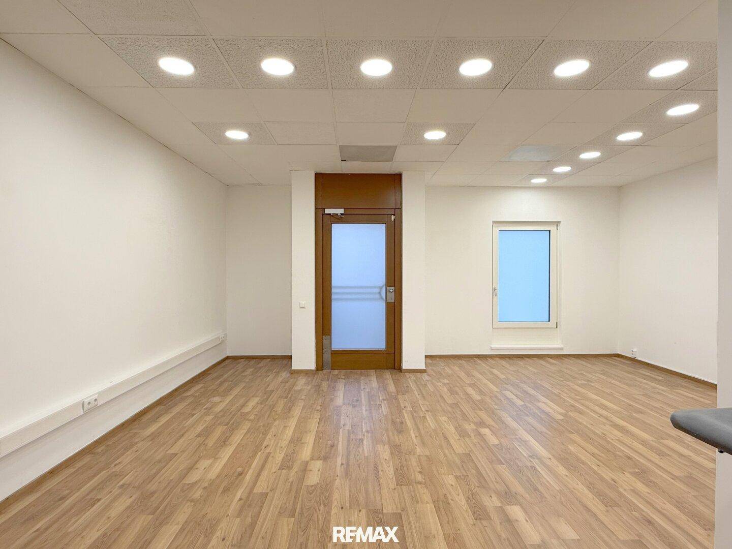 Heller, leerer Raum mit Holzboden, weißen Wänden und Deckenleuchten, ideal für ein Büro.
