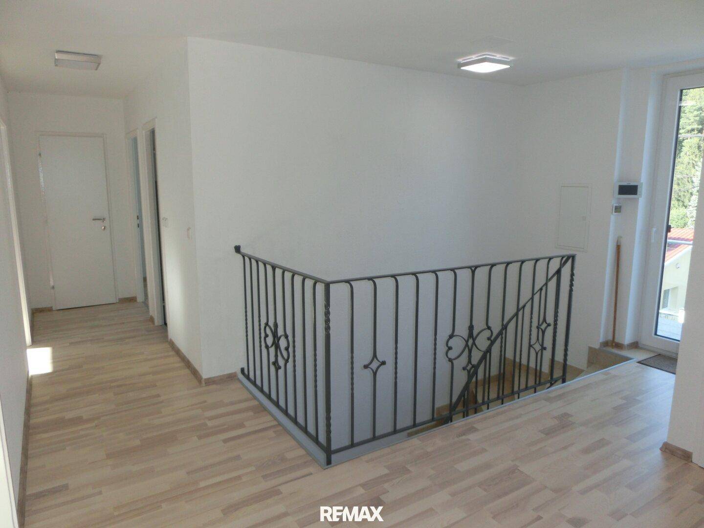 Heller Flur mit Holzboden und einem eleganten schmiedeeisernen Geländer zur Treppe.