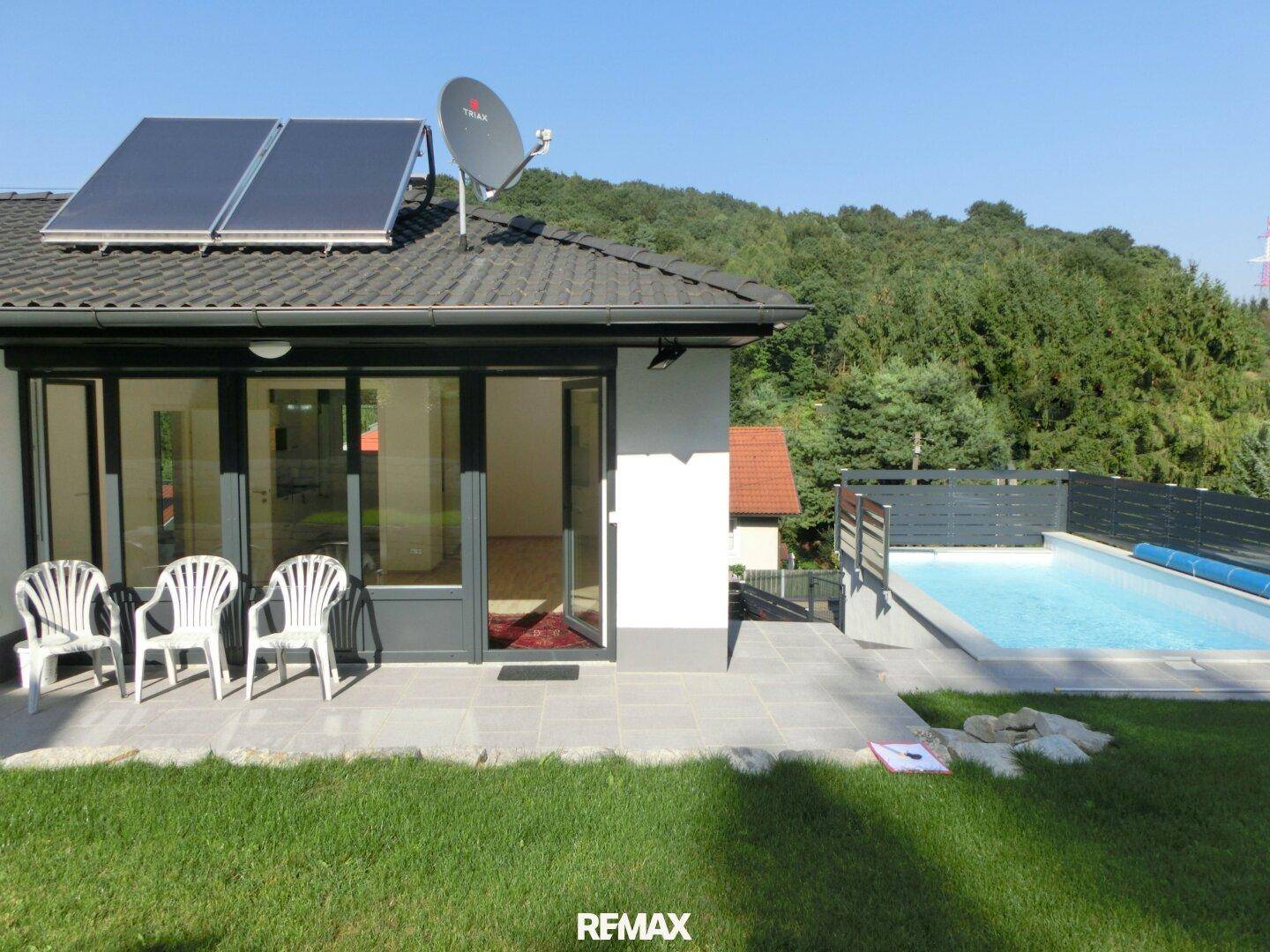 Haus mit großer Terrasse, Swimmingpool und Solaranlage auf dem Dach in ländlicher Umgebung.