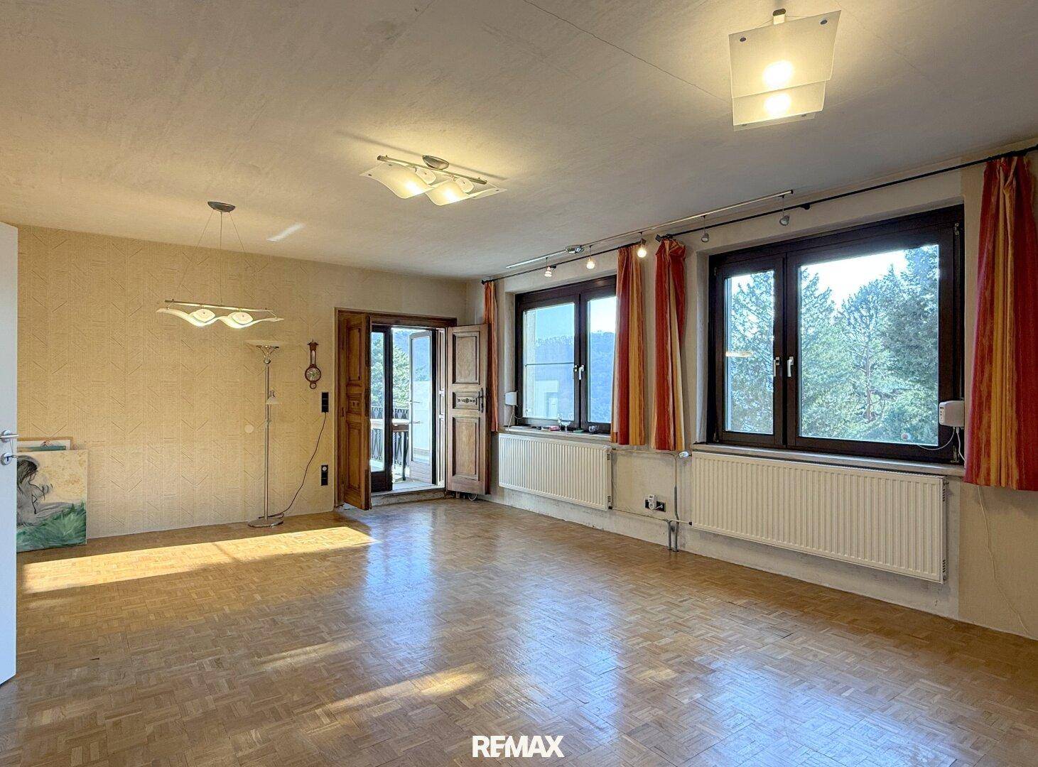 Geräumiges Wohnzimmer mit Parkettboden, großen Fenstern und Zugang zum Balkon.