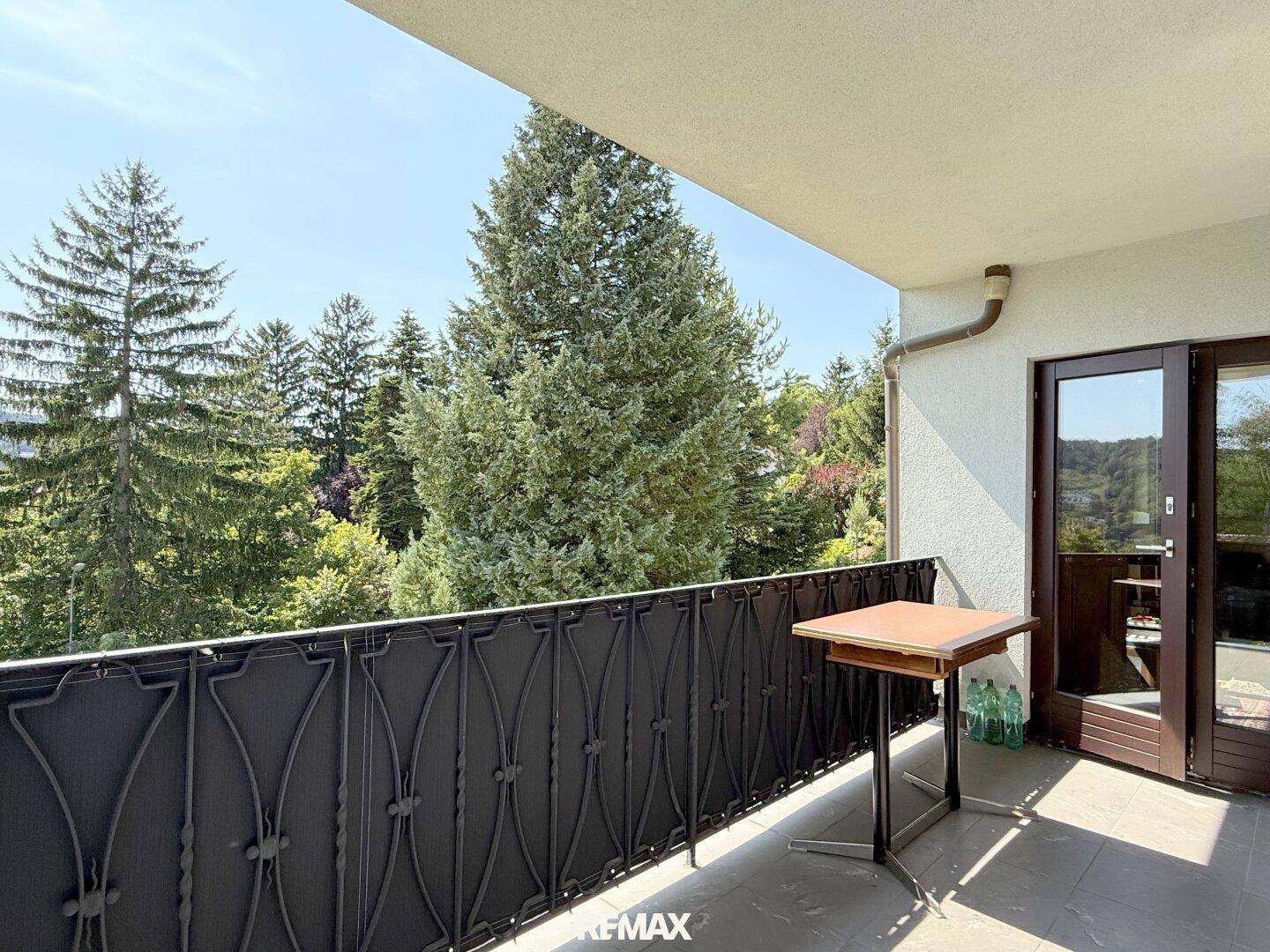 Sonniger Balkon mit schmiedeeisernem Geländer und Blick ins Grüne.