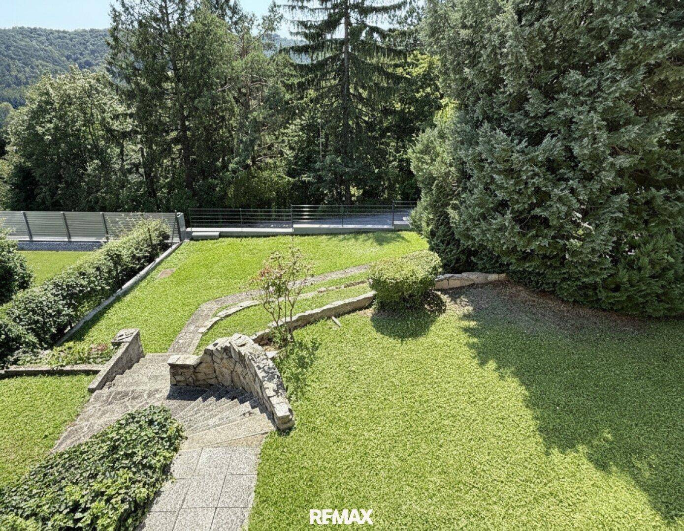 Terrassierter Gartenbereich mit Rasenflächen, Steinwegen und üppiger Bepflanzung.