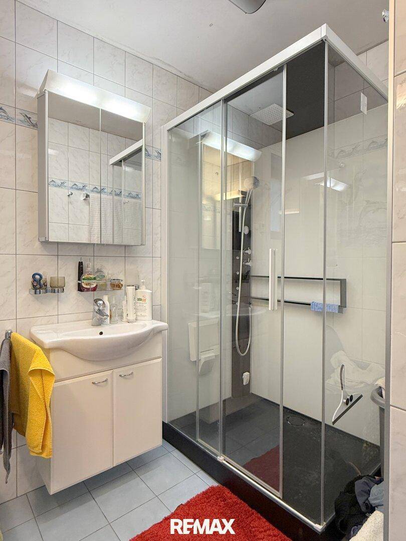 Gefliestes Badezimmer mit Duschkabine, Waschbecken und Spiegelschrank.