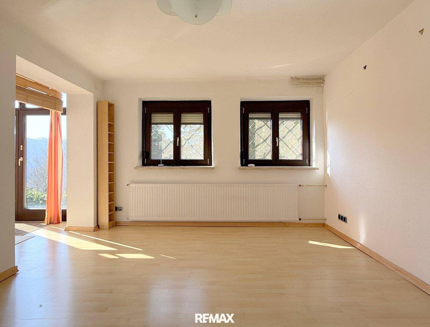 Helles Wohnzimmer mit Laminatboden und großen Fenstern, bereit zur Einrichtung.