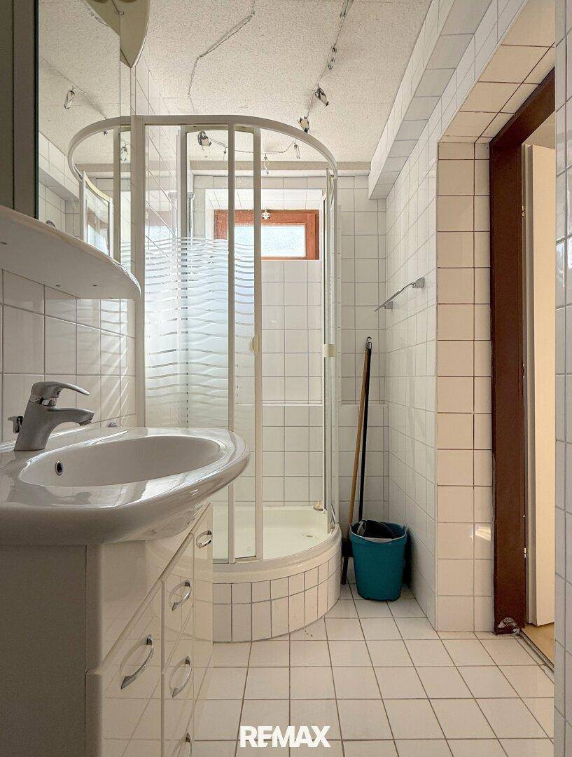 Gefliestes Badezimmer mit Duschkabine, Waschbecken und Fenster für Tageslicht.