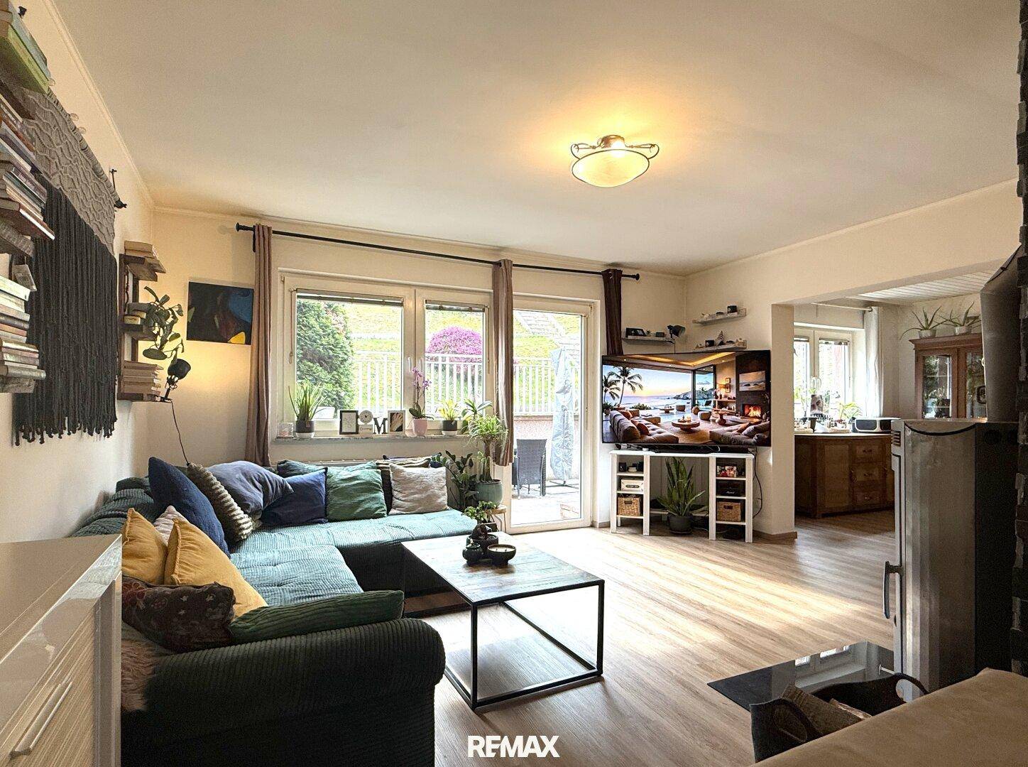 Helles Wohnzimmer mit großem Ecksofa, Kaminofen und Blick ins Grüne.