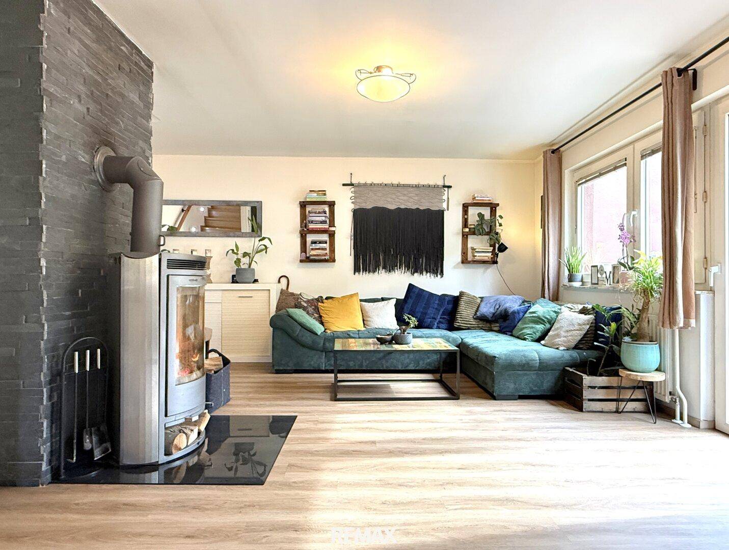 Geräumiges Wohnzimmer mit bequemer Sitzecke, Kaminofen und großen Fenstern.