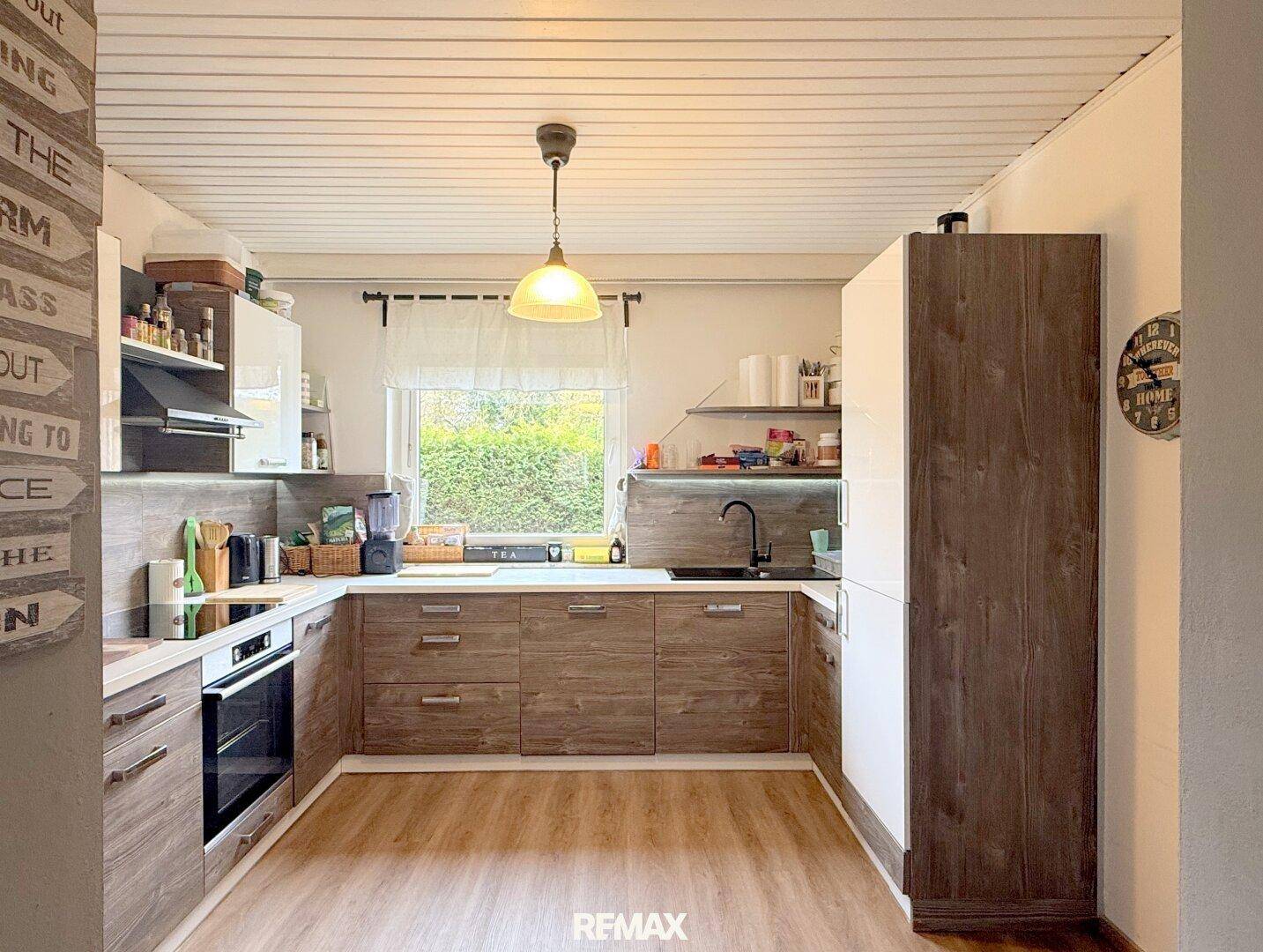 Funktionale Küche mit Holz- und weißen Schränken, Fenster und ausreichend Arbeitsfläche.
