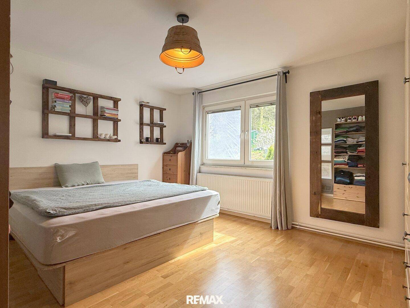 Schlafzimmer mit Holzbett, Parkettboden und Fenster mit Blick ins Grüne.
