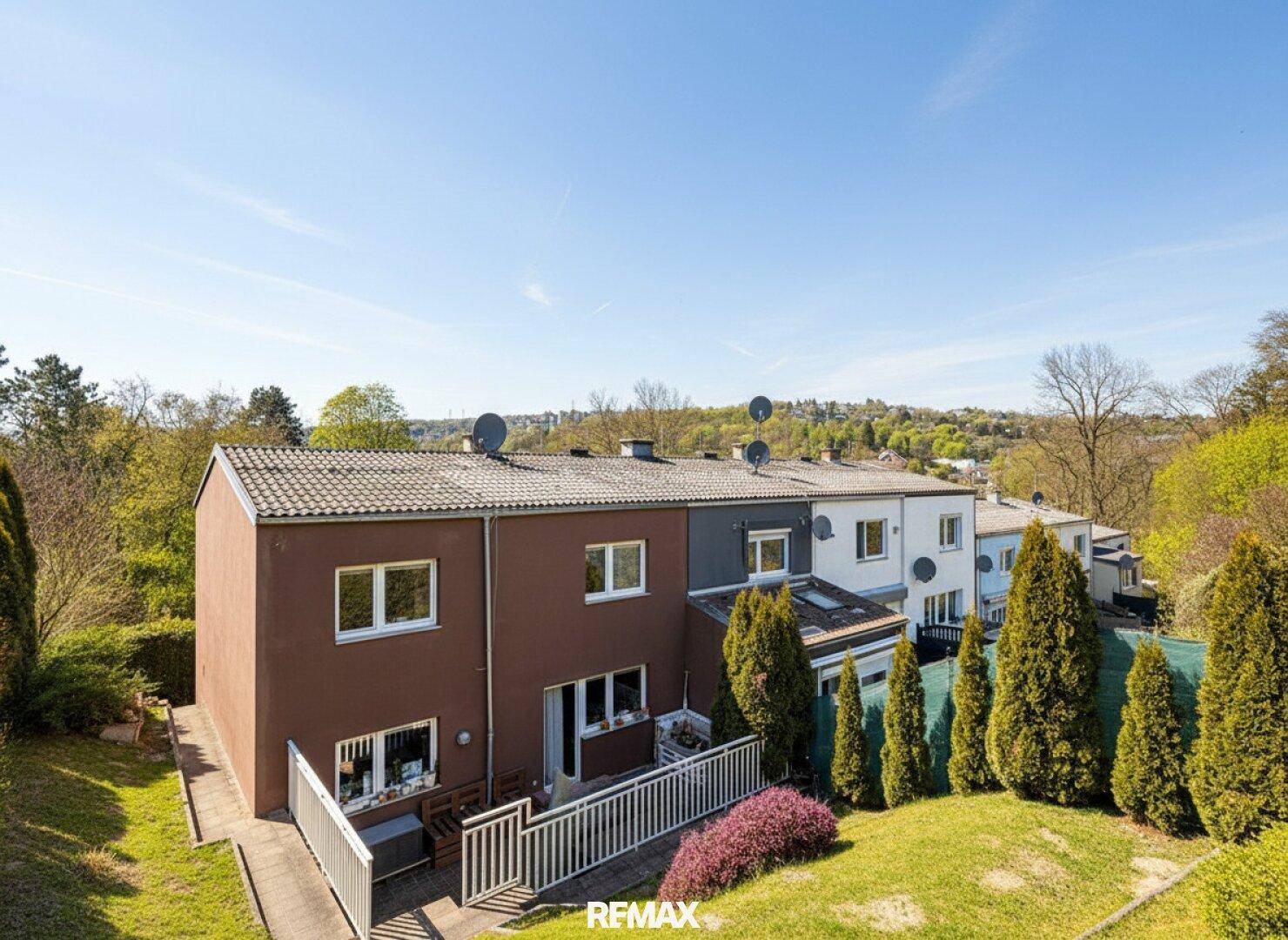Rückansicht einer Reihenhaussiedlung mit privaten Gärten und grüner Umgebung unter blauem Himmel.