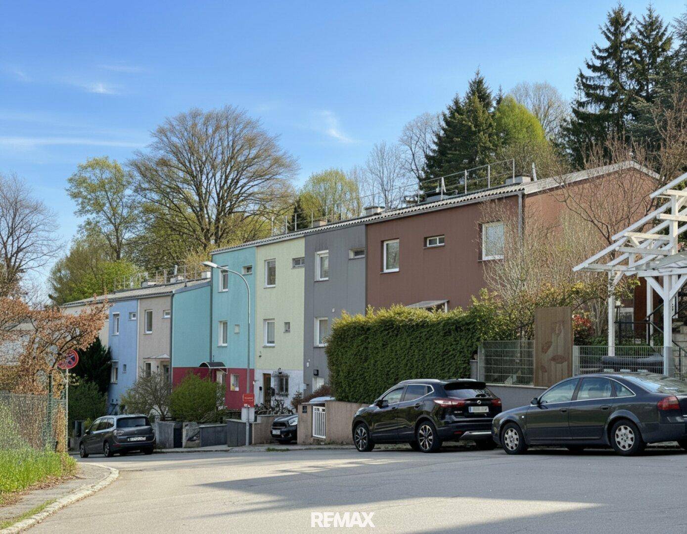 Blick auf eine Reihe bunter Reihenhäuser entlang einer Straße mit parkenden Autos.