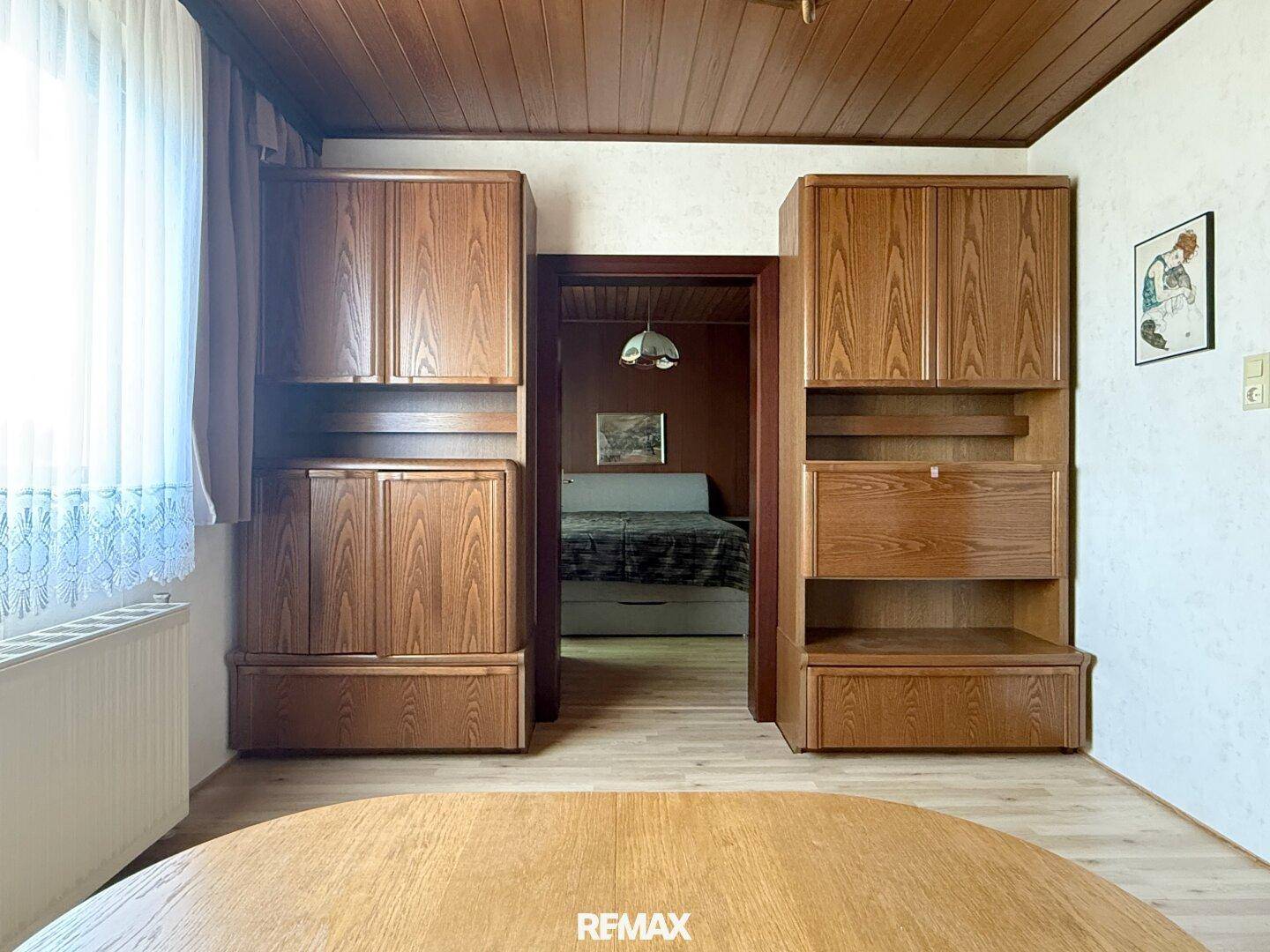 Wohnbereich mit Holzschränken und Durchgang zu einem weiteren Zimmer, typisch für den Stil der 80er Jahre.