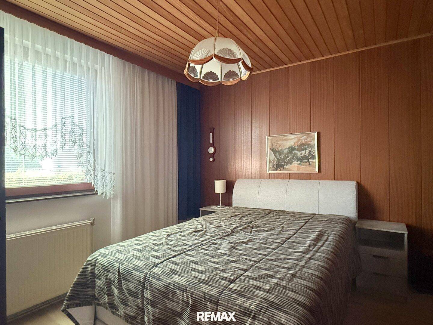 Schlafzimmer mit Holzwänden und -decke, einem Doppelbett und einem Fenster mit Vorhängen.