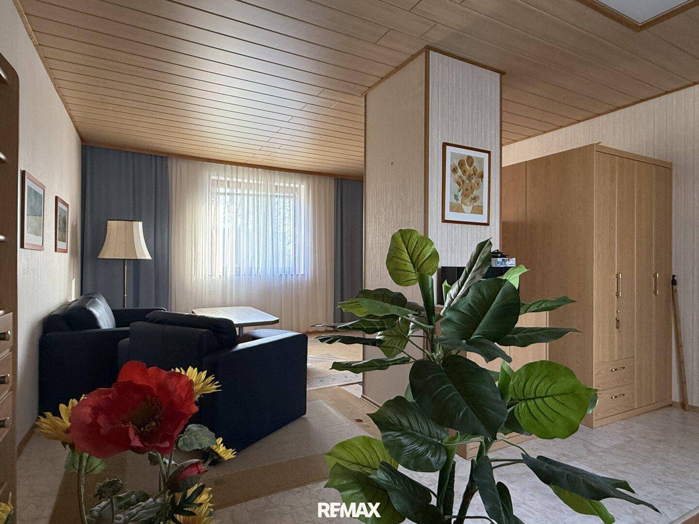 Geräumiges Wohnzimmer mit Holzdecke, beigen Tapeten und dunklen Sofas.