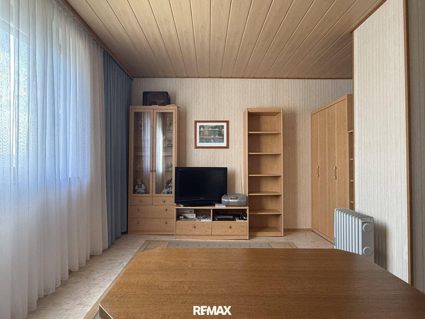 Wohnzimmer mit TV-Möbeln, Regalen und einem Heizkörper unter dem Fenster.