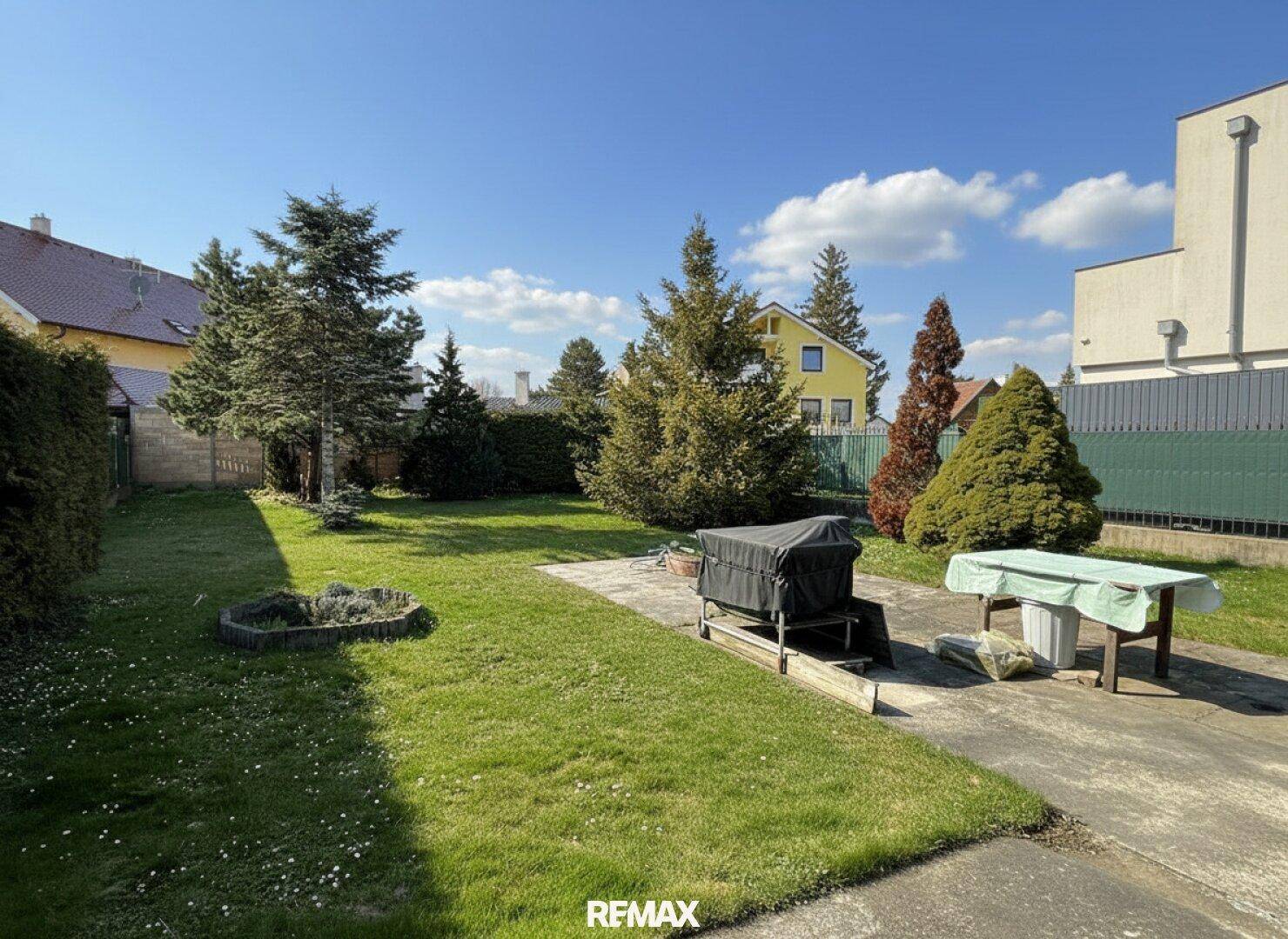 Großer, gepflegter Garten mit Rasenfläche, Bäumen und einer gepflasterten Terrasse.
