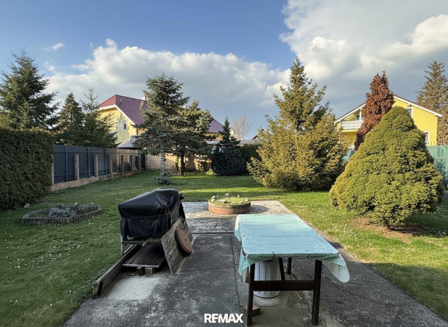 Sonniger Garten mit Rasen, Bäumen und einem Bereich für Grillabende.