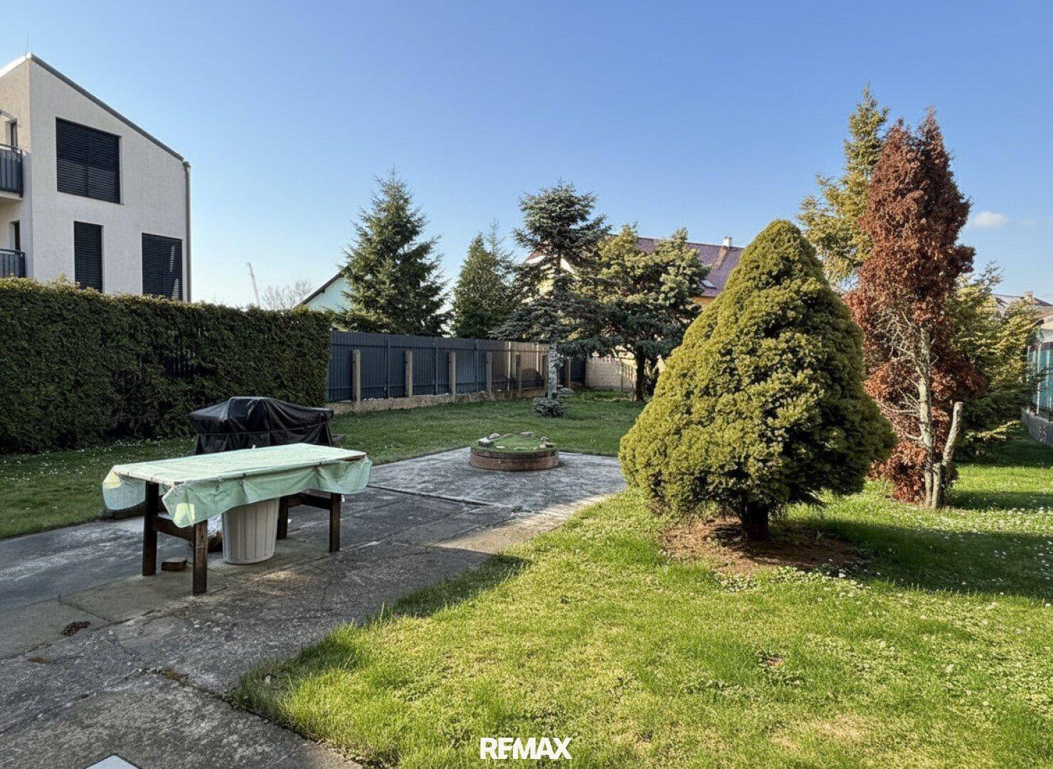 Weitläufiger Garten mit Rasenfläche, Bäumen und einer gepflasterten Fläche für Outdoor-Aktivitäten.