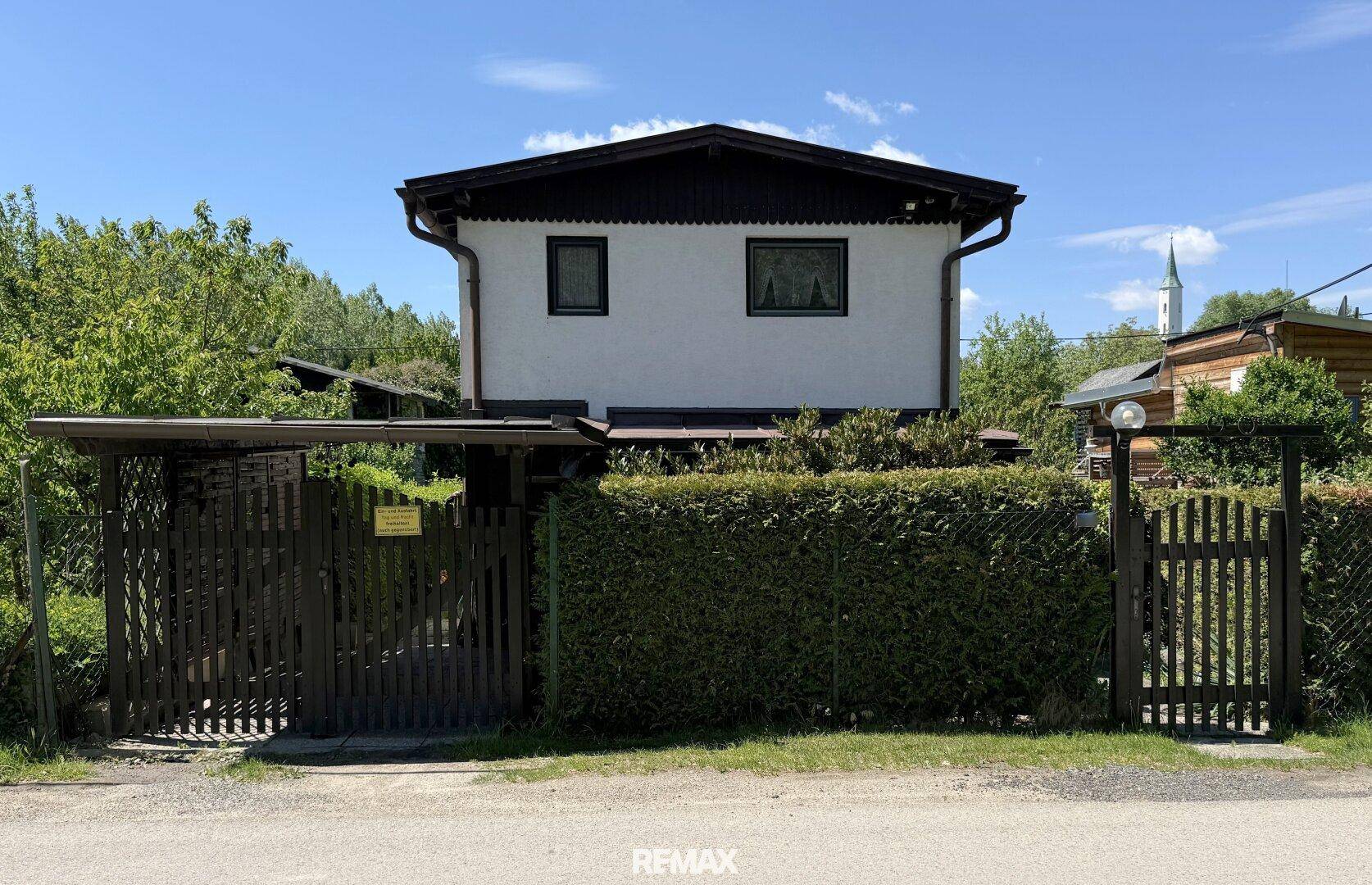 Vorderansicht des Hauses mit weißer Fassade, dunklem Dach und Holzzaun.