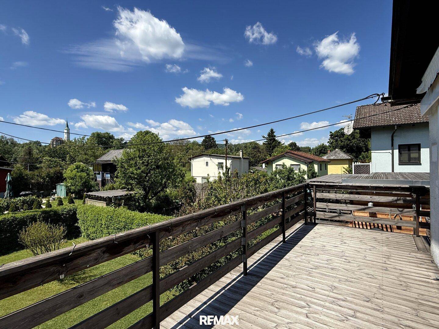 Geräumiger Holzbalkon mit Blick auf die grüne Umgebung und Nachbarhäuser.