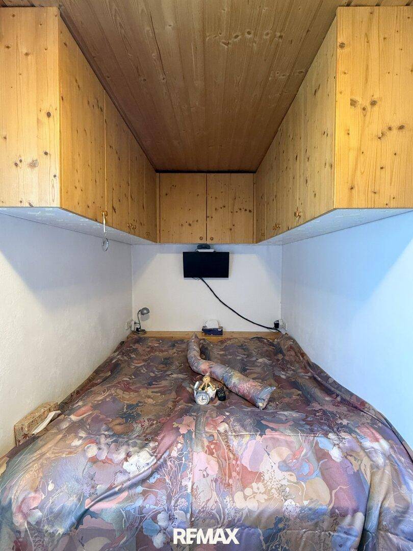 Schlafzimmer mit Holzwänden und -decke, ausgestattet mit einem Doppelbett und Stauraum.