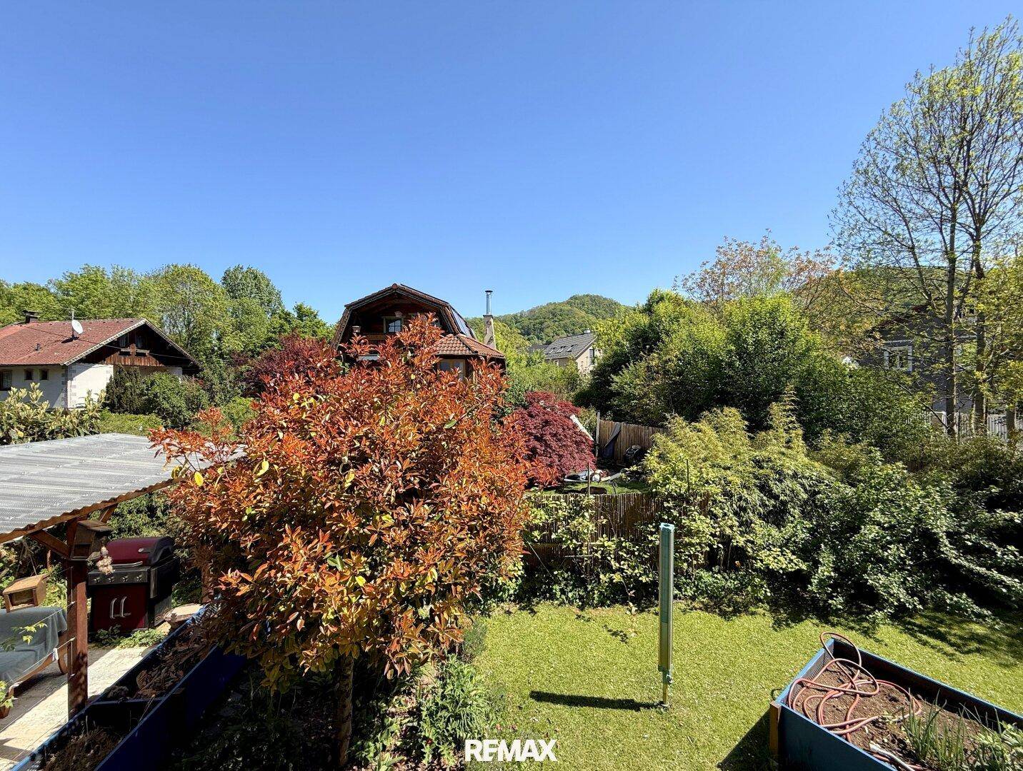 Sonniger Gartenbereich mit bunten Bäumen und Sträuchern sowie Hochbeeten für den Anbau.