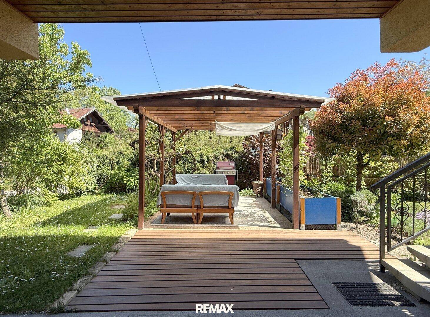 Einladender Gartenbereich mit Holzterrasse, Pergola und Sitzgelegenheiten im Grünen.