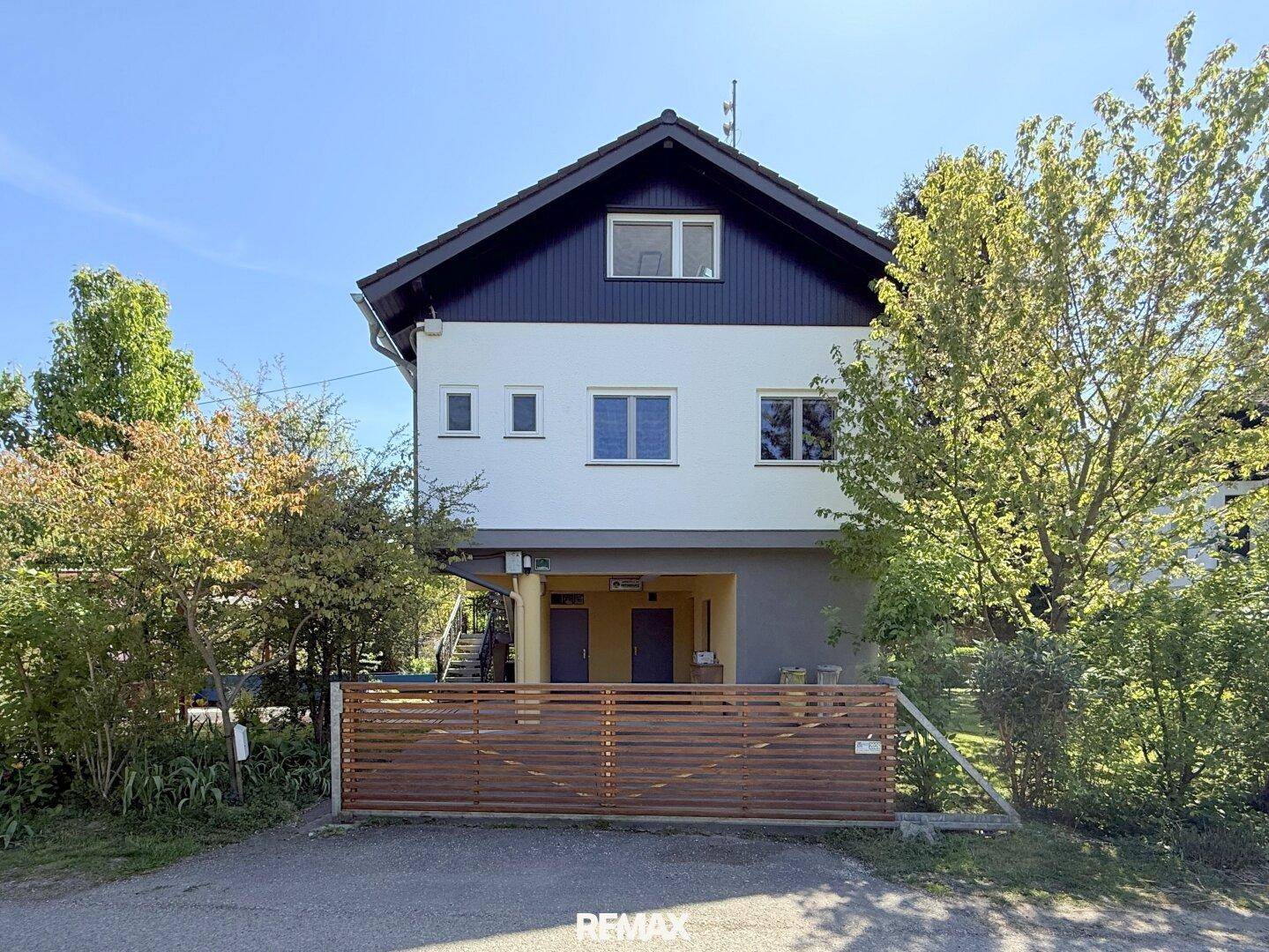 Ansicht der Hausfassade mit Fenstern und Eingangsbereichen, umgeben von Bäumen.