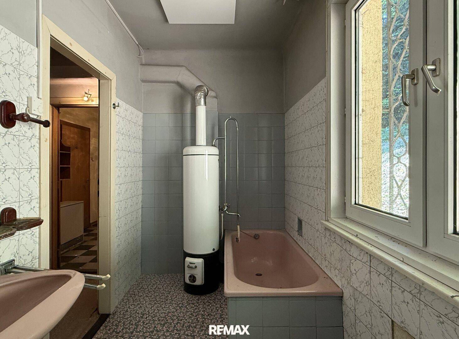 Badezimmer mit rosa Badewanne, Warmwasserboiler und gefliesten Wänden, typisch für die 80er Jahre.