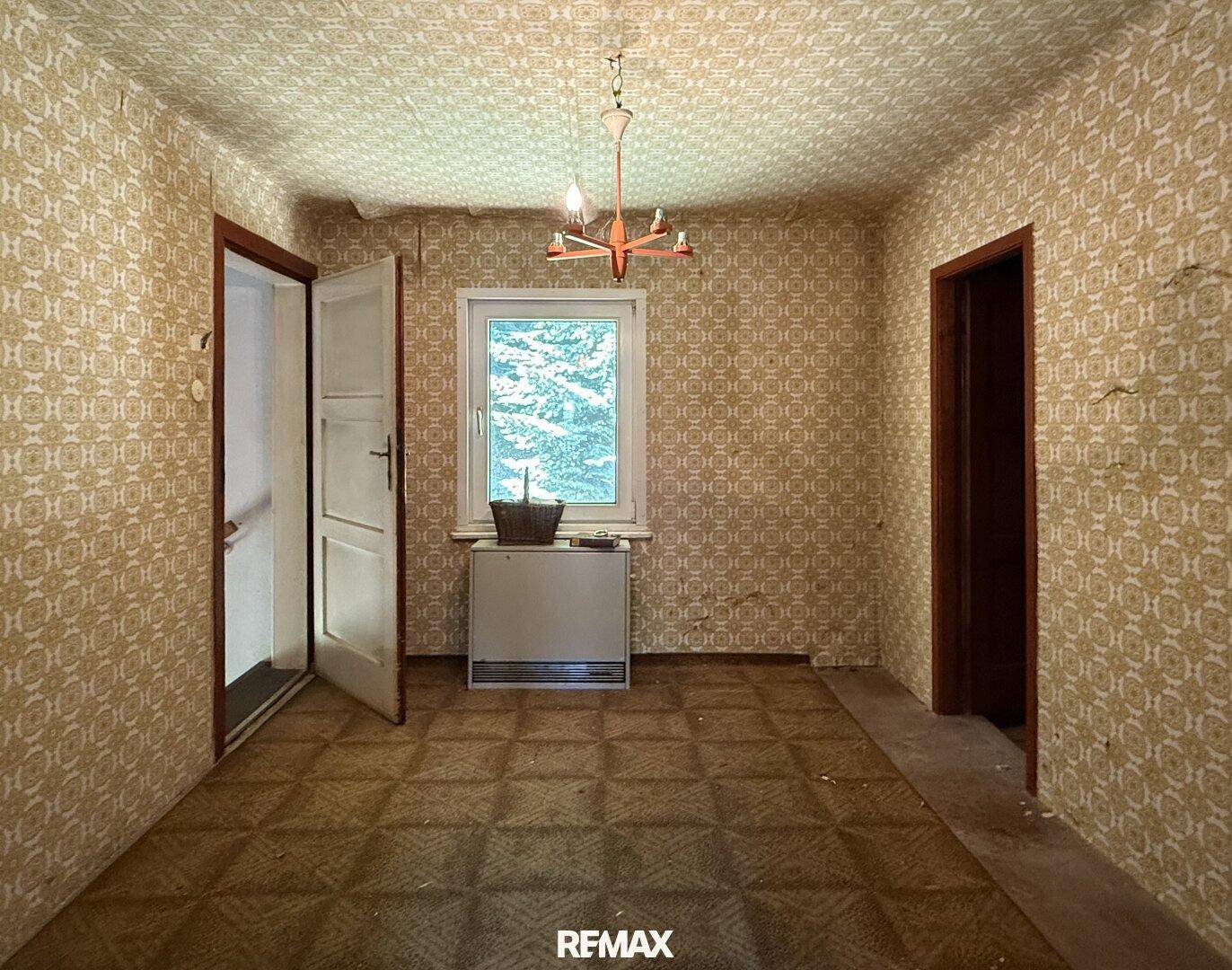 Zimmer mit gemusterter Tapete und Fenster, das viel natürliches Licht hereinlässt.