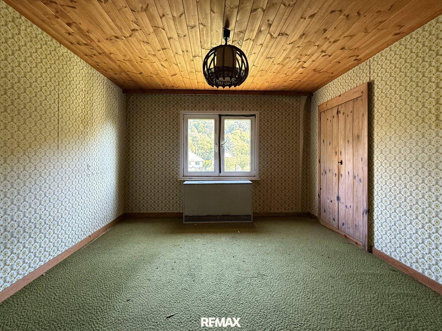 Schlafzimmer mit gemusterter Tapete, Holzdecke und grünem Teppichboden, bietet eine ruhige Atmosphäre.