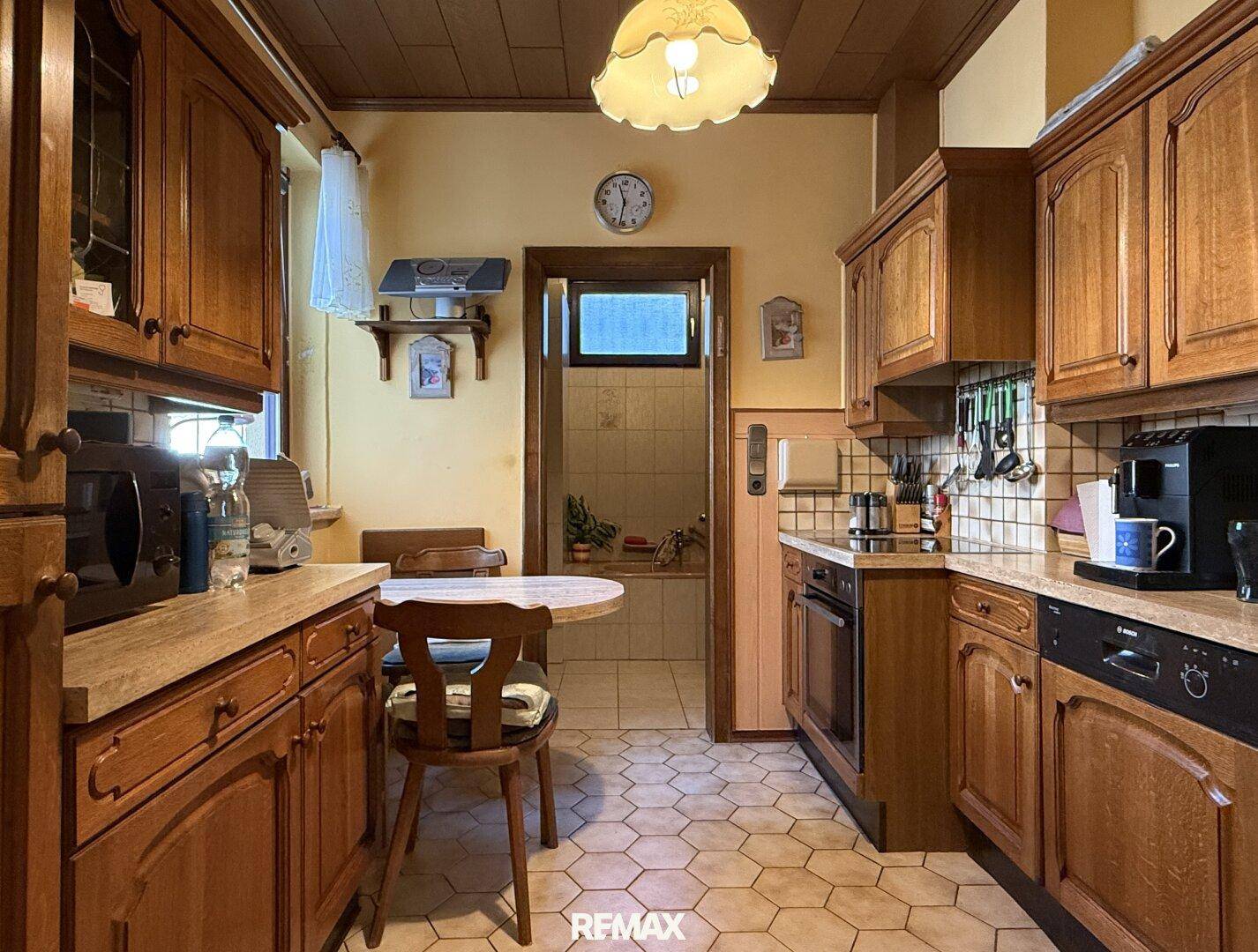 Gemütliche Küche im Landhausstil mit Holzeinbauten, Essbereich und Blick in ein angrenzendes Bad.
