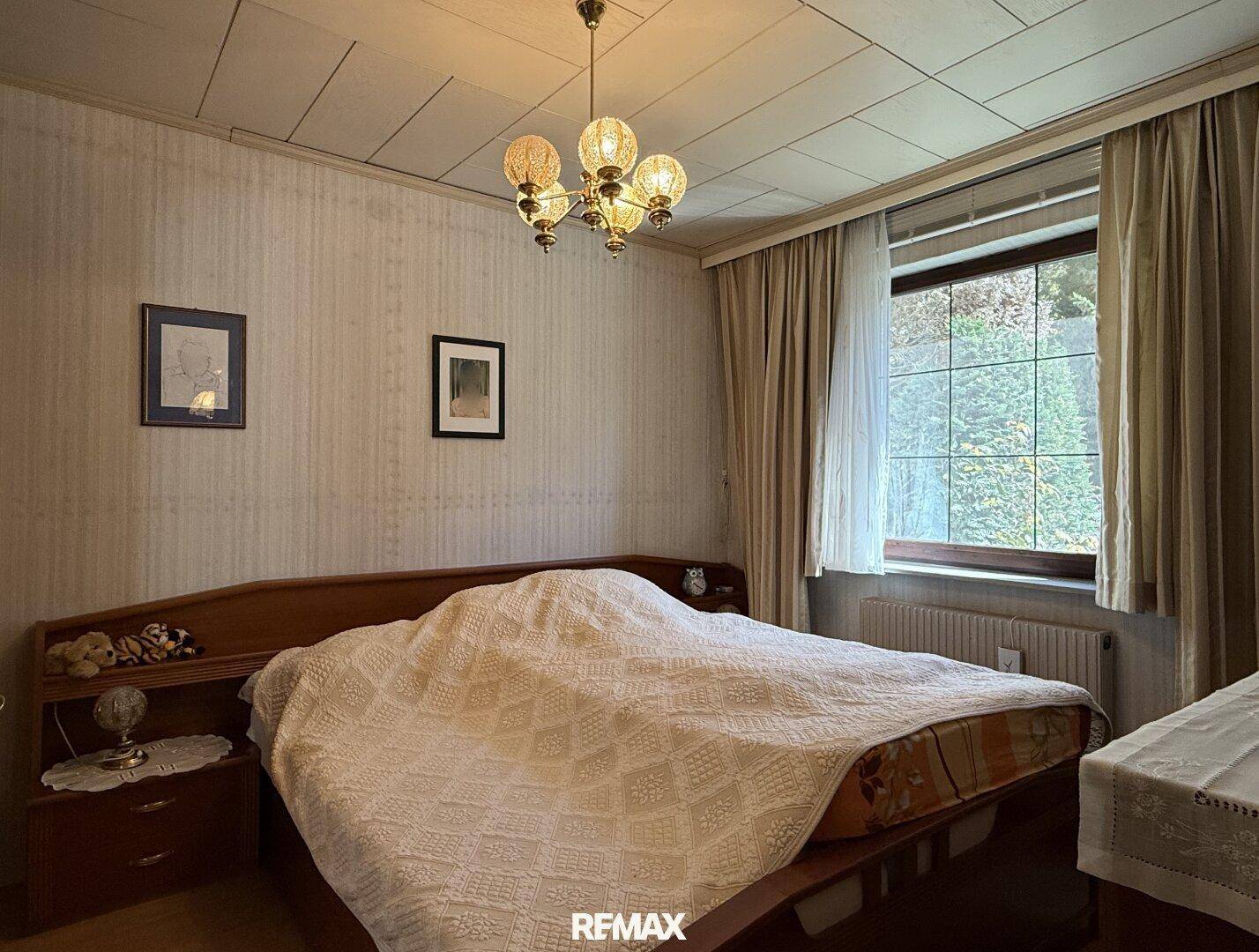 Schlafzimmer mit Doppelbett, Holzdecke und Fenster mit Blick ins Grüne.