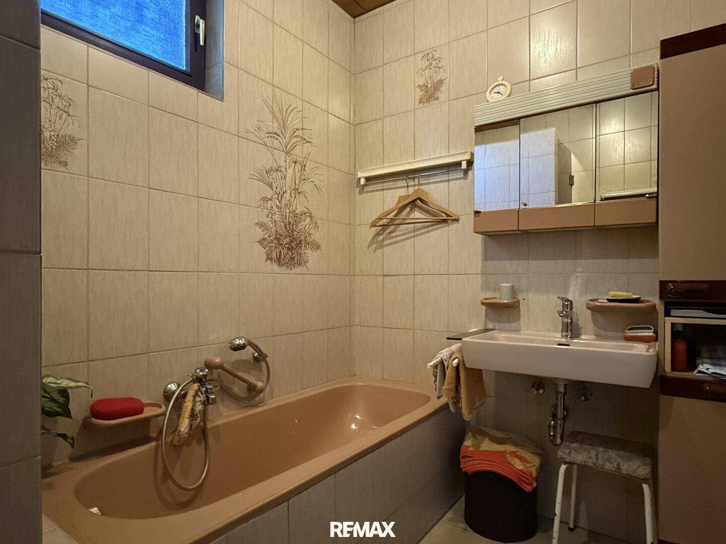 Badezimmer im 80er-Jahre-Stil mit beiger Badewanne, Fliesen und Fenster.
