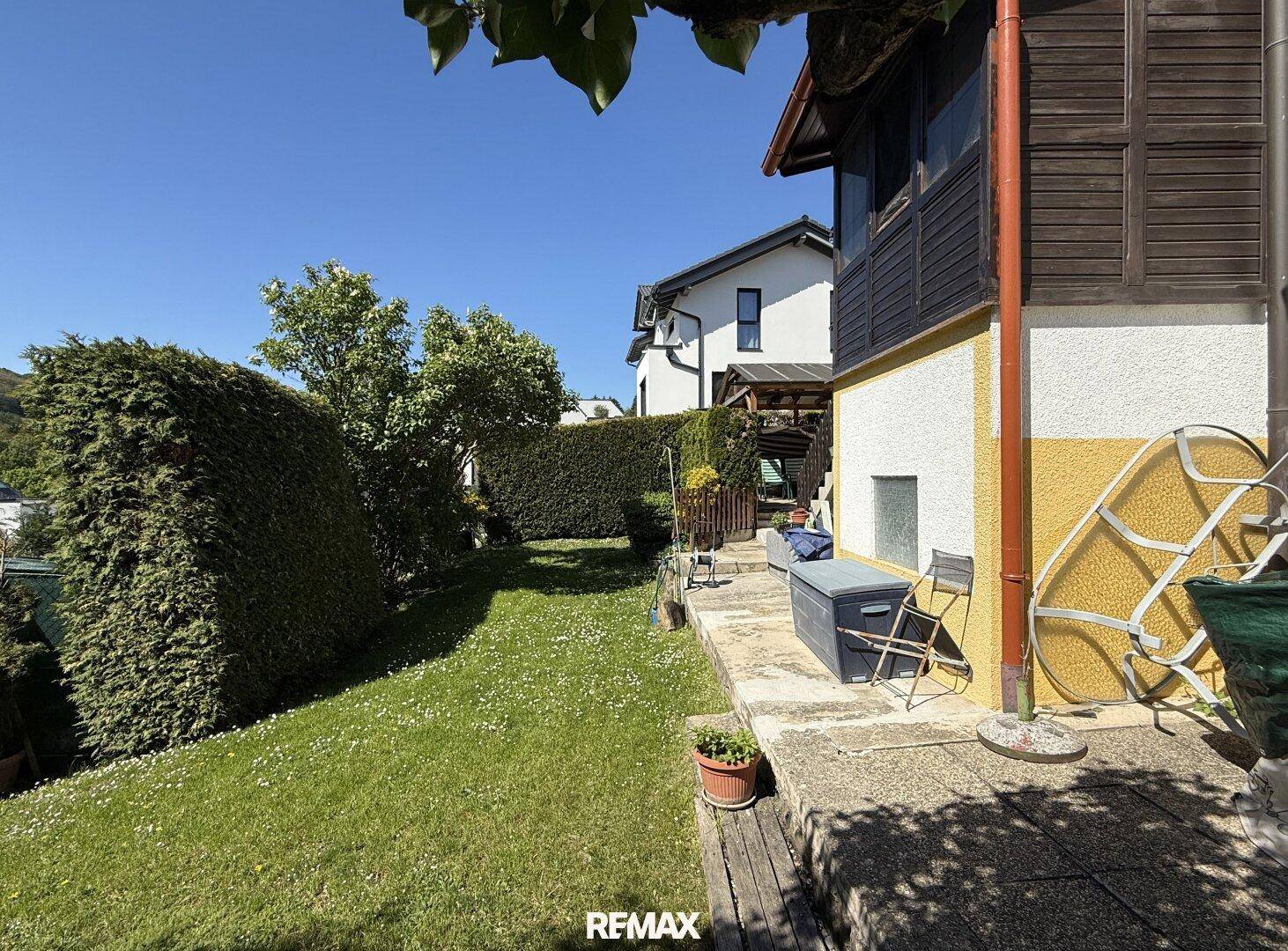 Seitlicher Gartenbereich mit Rasenfläche, Hecke und Terrasse am Haus.