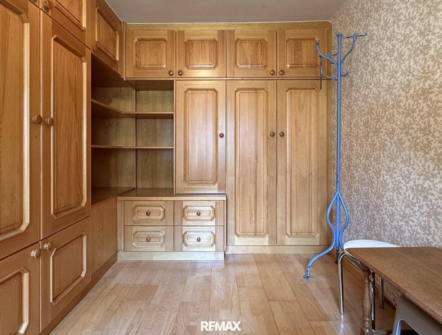 Schlafzimmer mit umfangreichen Einbauschränken aus Holz und gemusterter Tapete.