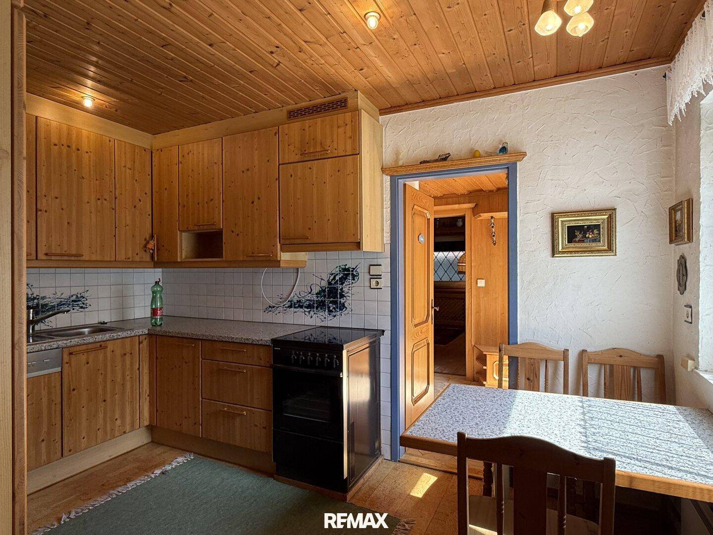 Funktionale Küche im Landhausstil mit Holzschränken, Elektroherd und Essbereich.